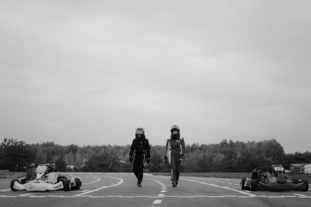 Two kart racers in full gear walking on a racetrack, emphasizing karting sportsmanship.